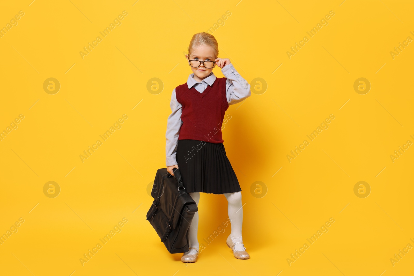 Photo of Little girl with glasses and briefcase on orange background. Dreaming of future profession