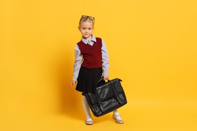 Photo of Little girl with glasses and briefcase on orange background. Dreaming of future profession