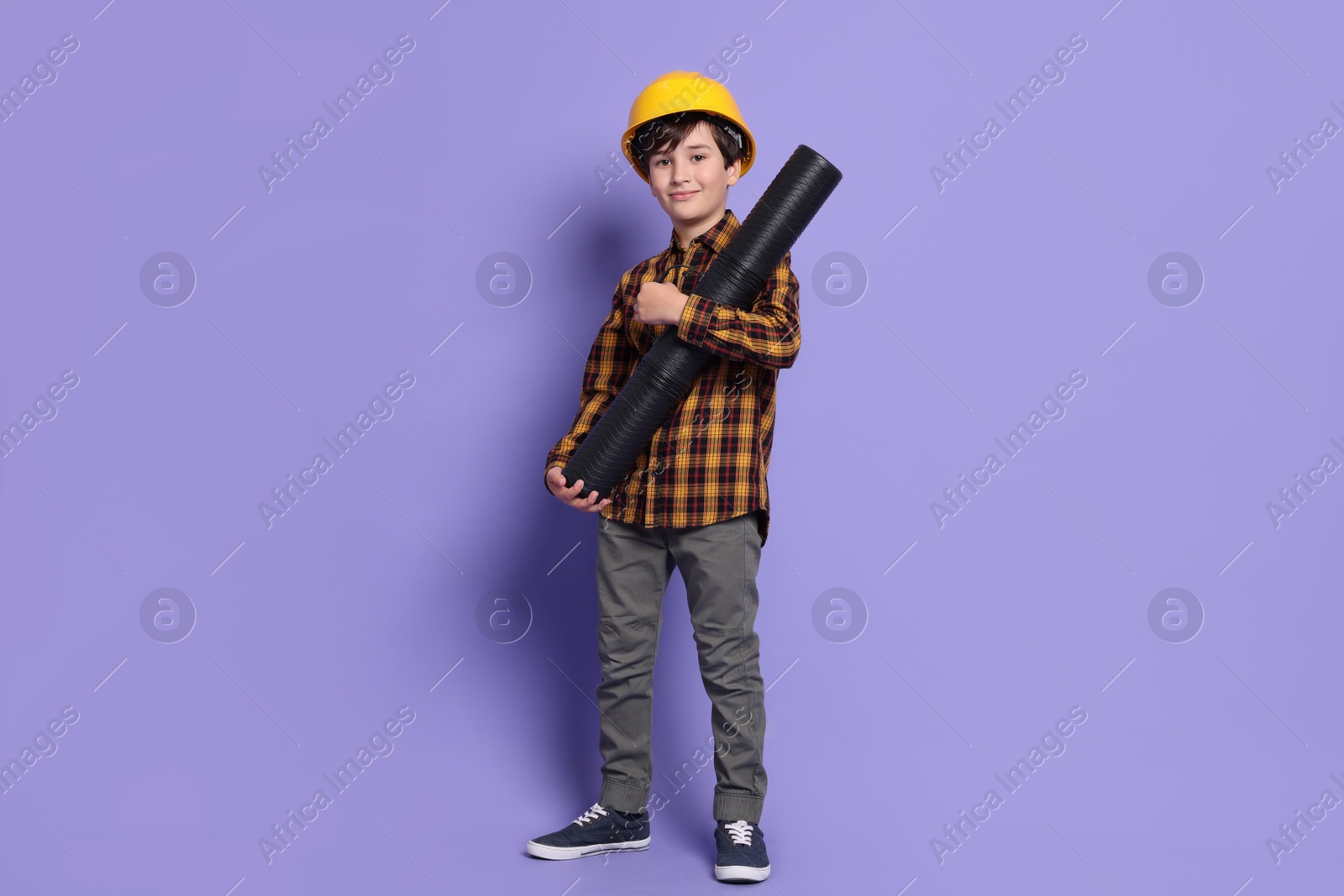 Photo of Boy with blueprint tube pretending to be architect on violet background. Dreaming of future profession