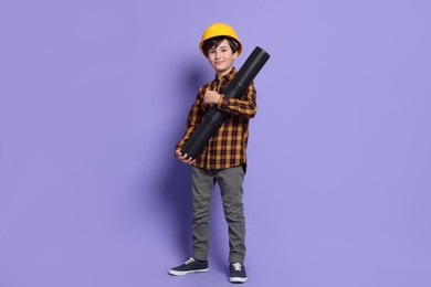 Photo of Boy with blueprint tube pretending to be architect on violet background. Dreaming of future profession