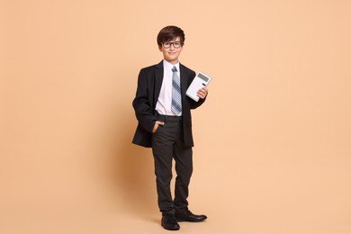 Photo of Boy with calculator pretending to be accountant on beige background. Dreaming of future profession