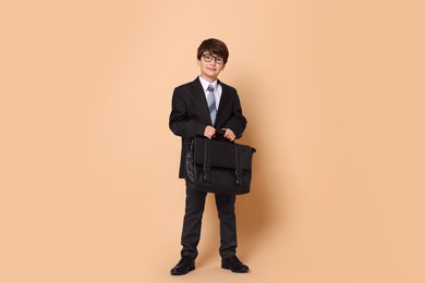 Photo of Boy in suit pretending to be businessman on beige background. Dreaming of future profession