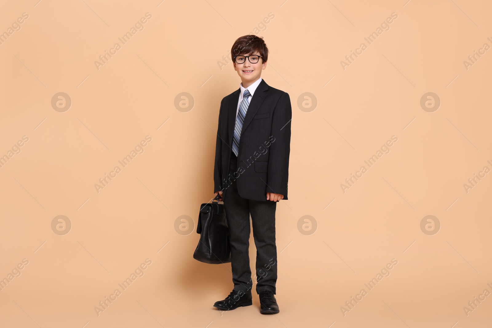 Photo of Boy in suit pretending to be businessman on beige background. Dreaming of future profession