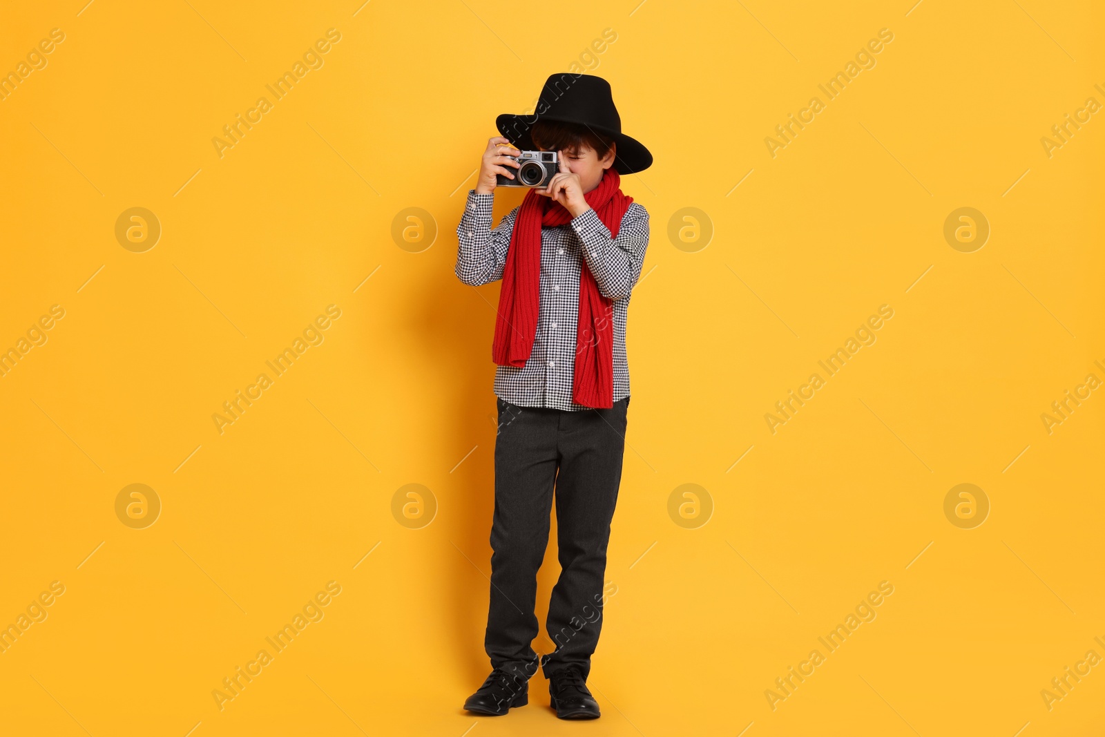 Photo of Boy with camera pretending to be photographer on orange background. Dreaming of future profession