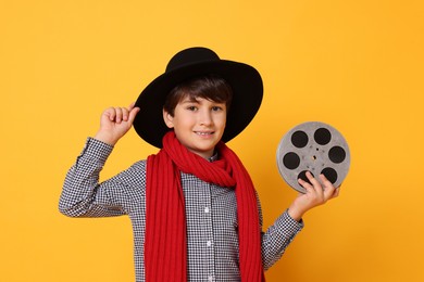 Photo of Boy with film reel pretending to be movie director on orange background. Dreaming of future profession