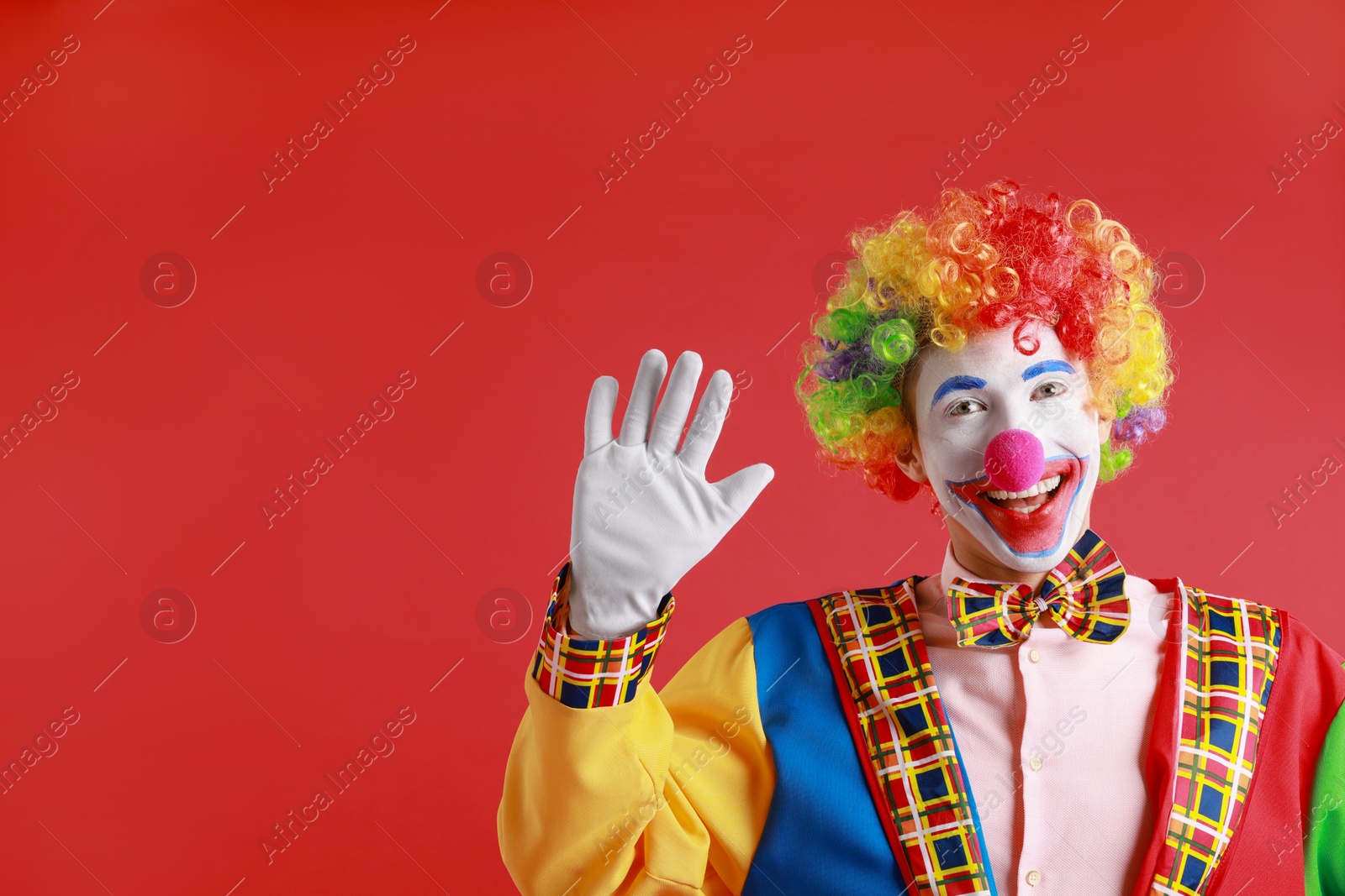 Photo of Portrait of happy clown waving on red background, space for text