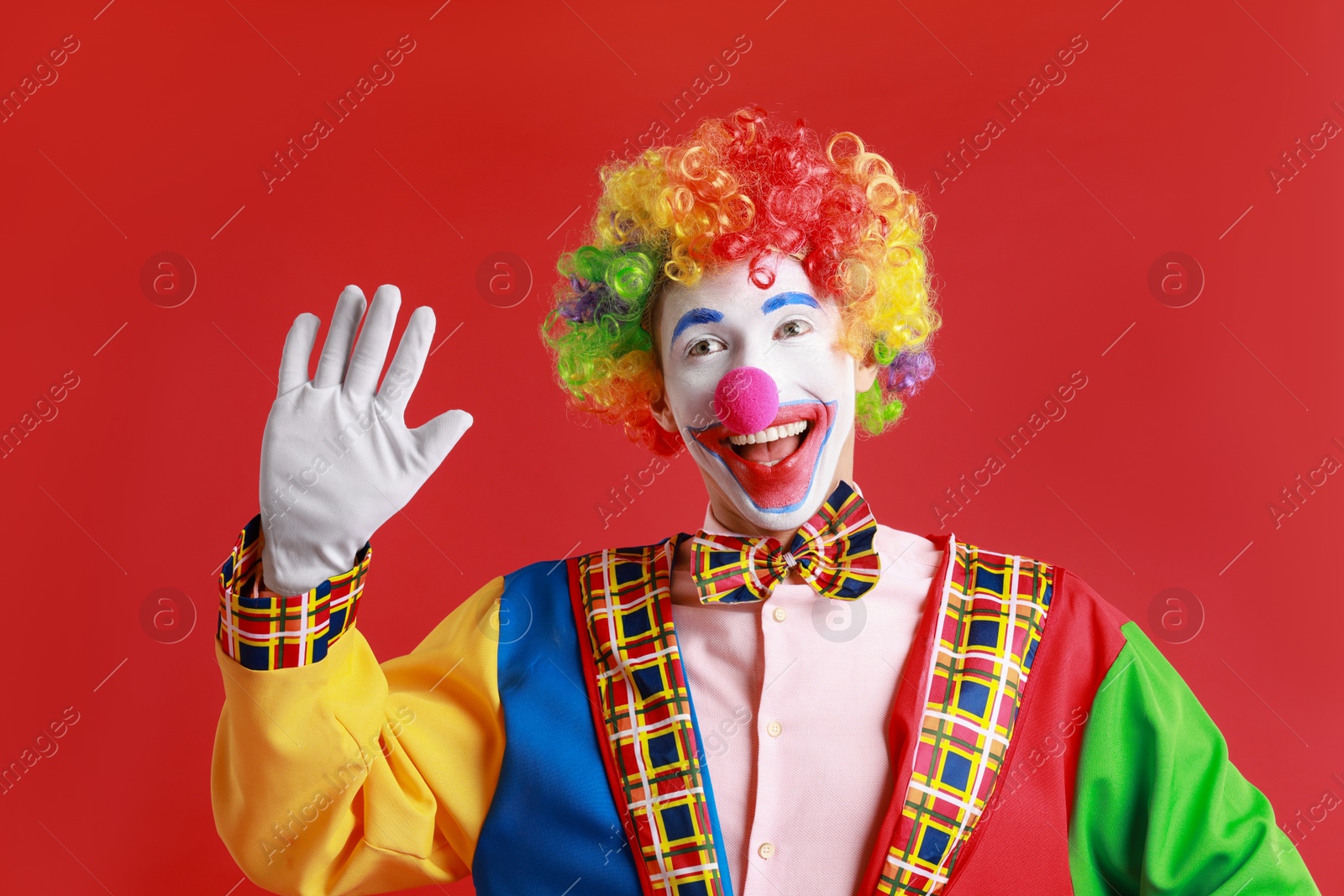 Photo of Portrait of happy clown waving on red background