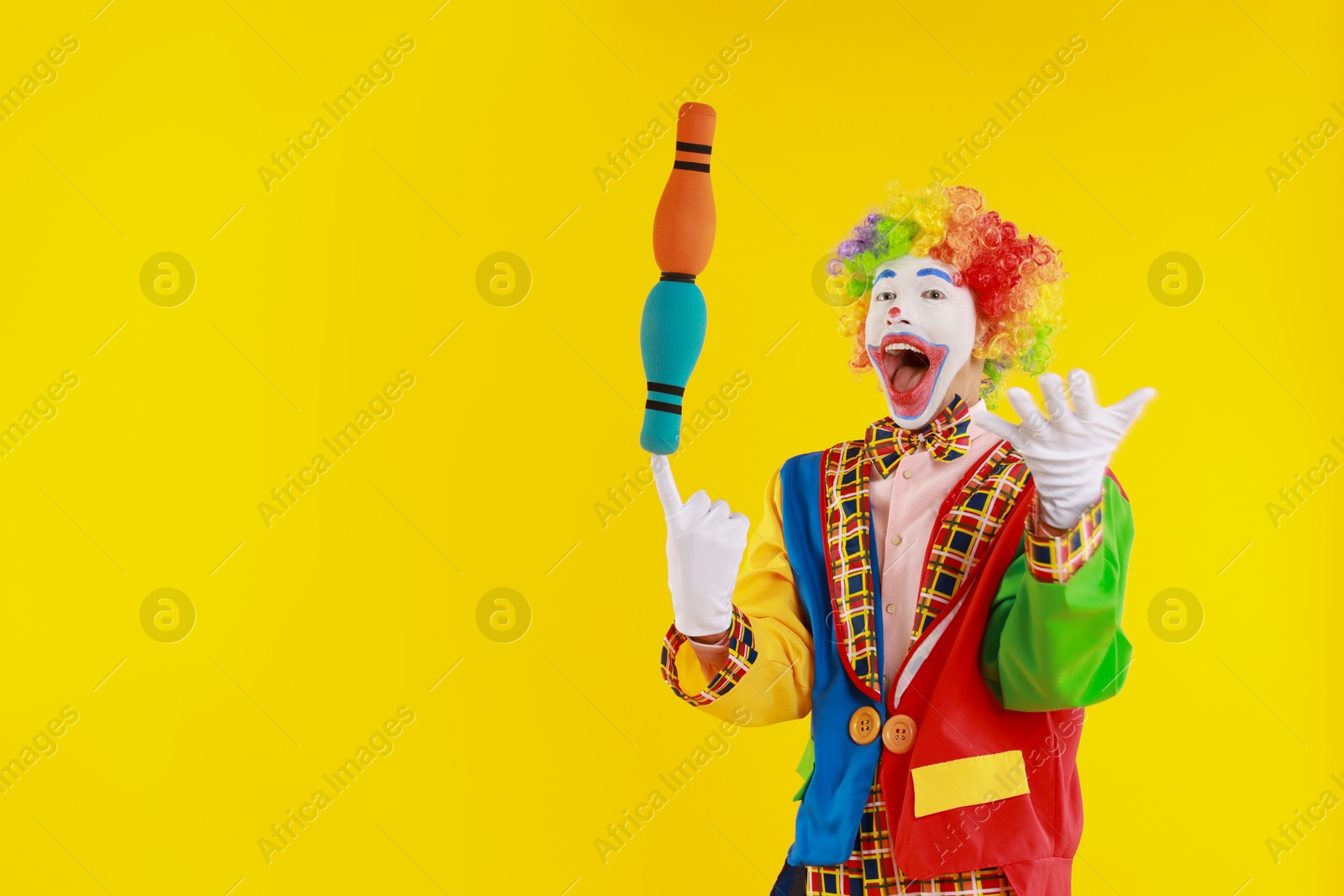 Photo of Emotional clown with juggling clubs on yellow background, space for text