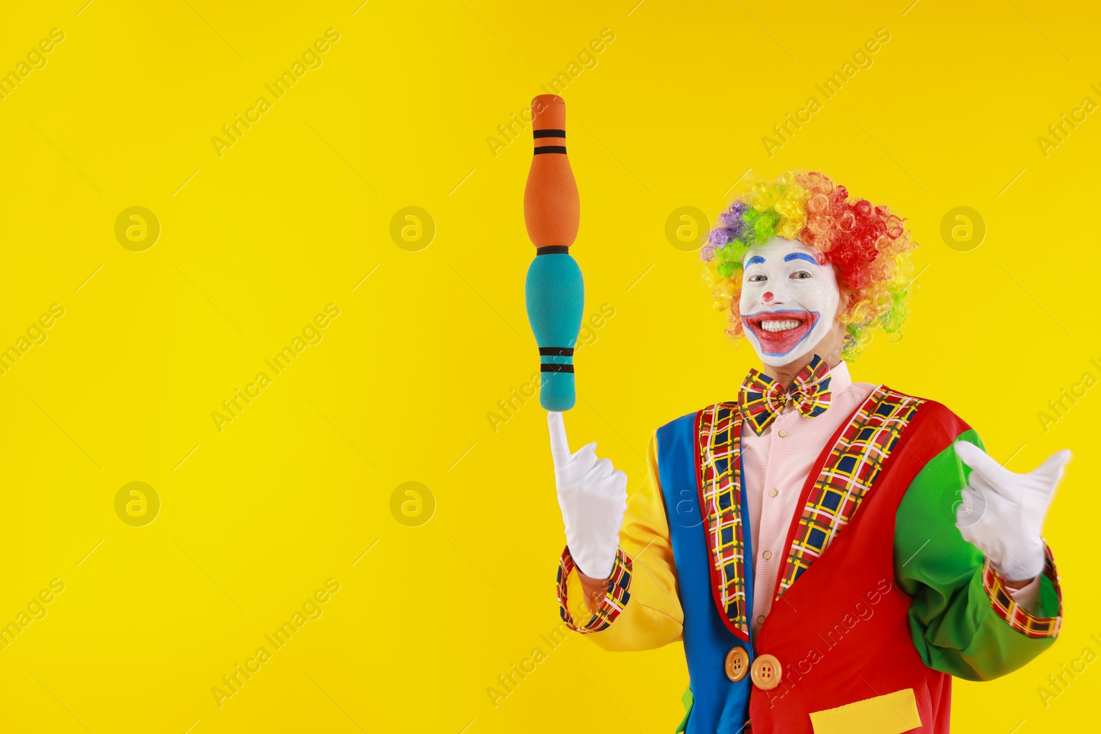 Photo of Happy clown with juggling clubs on yellow background, space for text