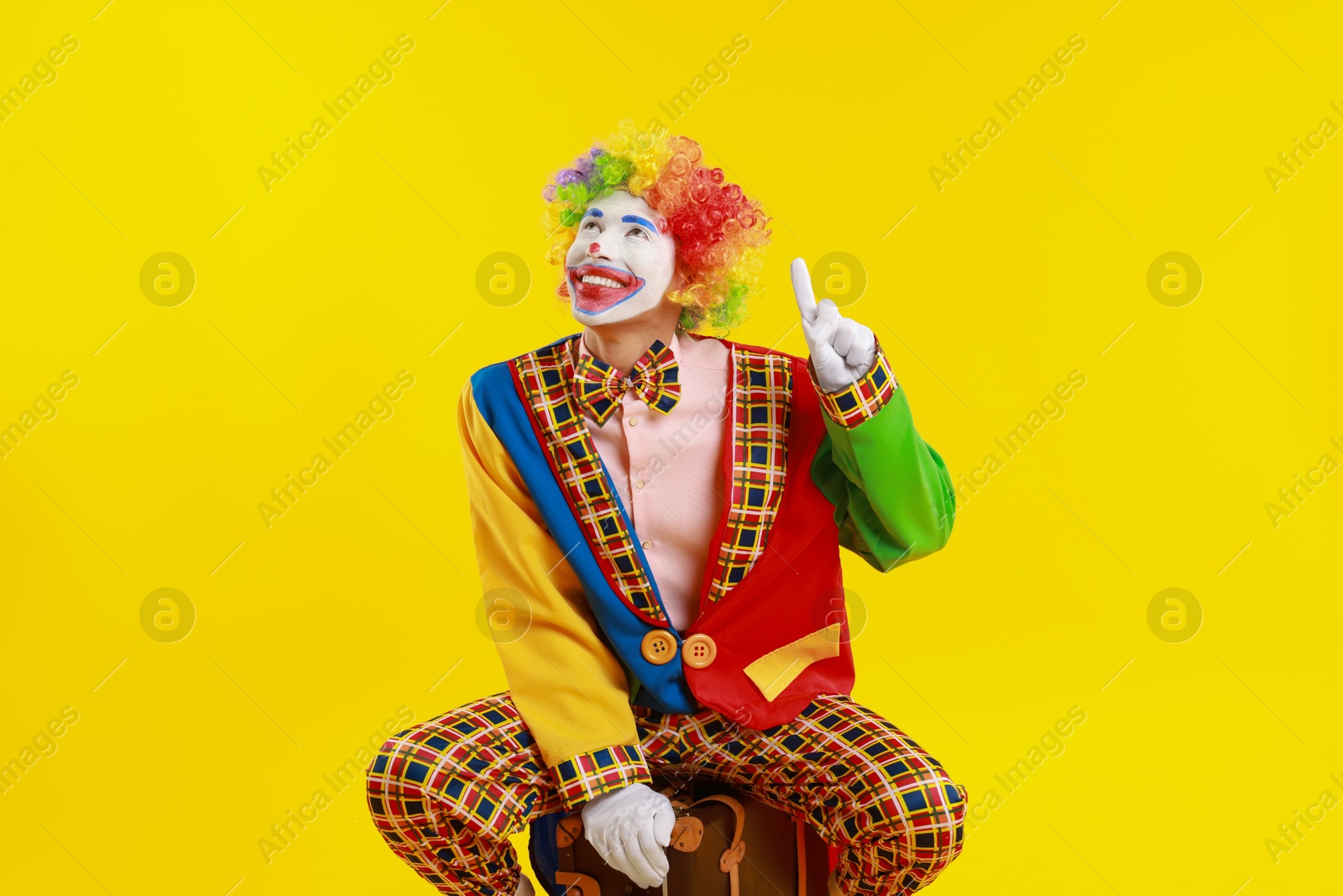 Photo of Happy clown with suitcase on yellow background