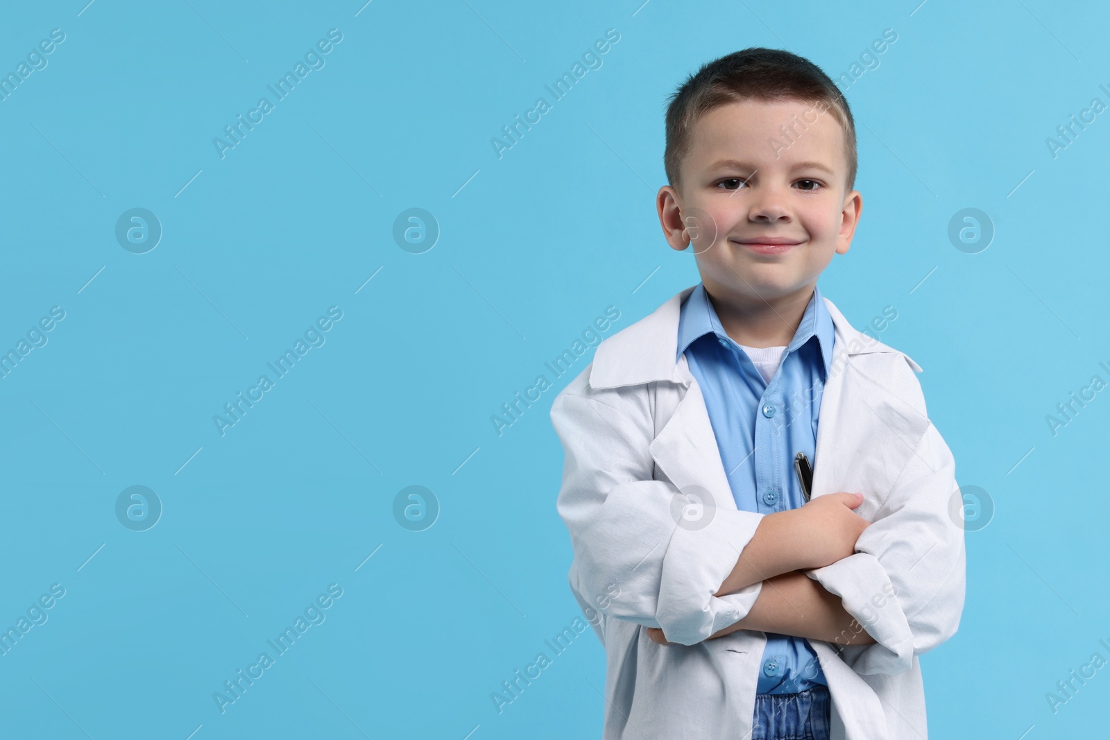 Photo of Little boy pretending to be doctor on light blue background, space for text. Dreaming of future profession