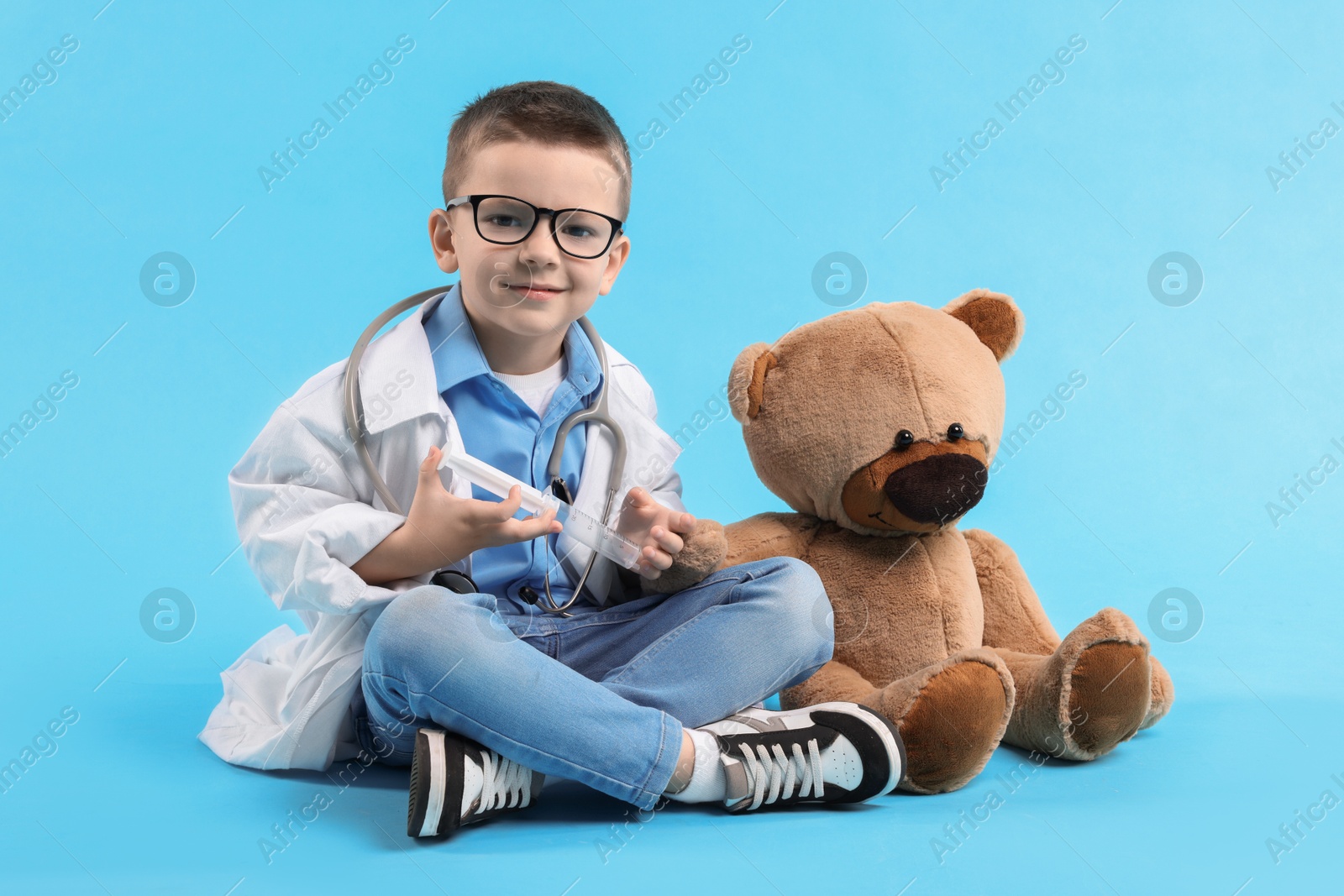 Photo of Little boy with stethoscope and toy pretending to be doctor on light blue background. Dreaming of future profession