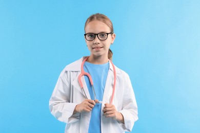 Photo of Girl with stethoscope pretending to be doctor on light blue background. Dreaming of future profession