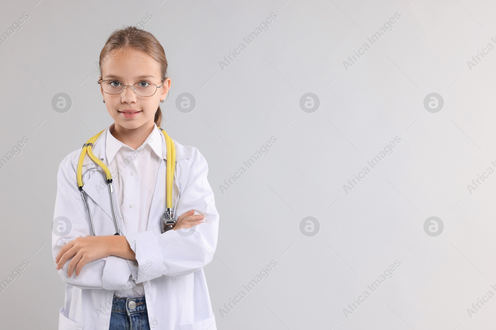 Photo of Girl with stethoscope pretending to be doctor on light grey background, space for text. Dreaming of future profession