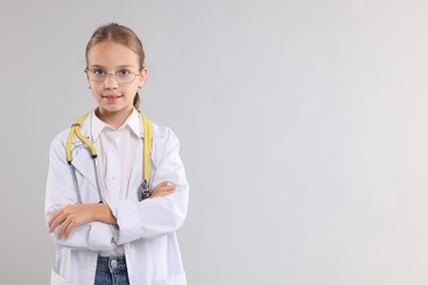 Girl with stethoscope pretending to be doctor on light grey background, space for text. Dreaming of future profession