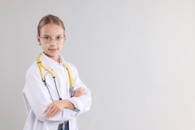 Photo of Girl with stethoscope pretending to be doctor on light grey background, space for text. Dreaming of future profession