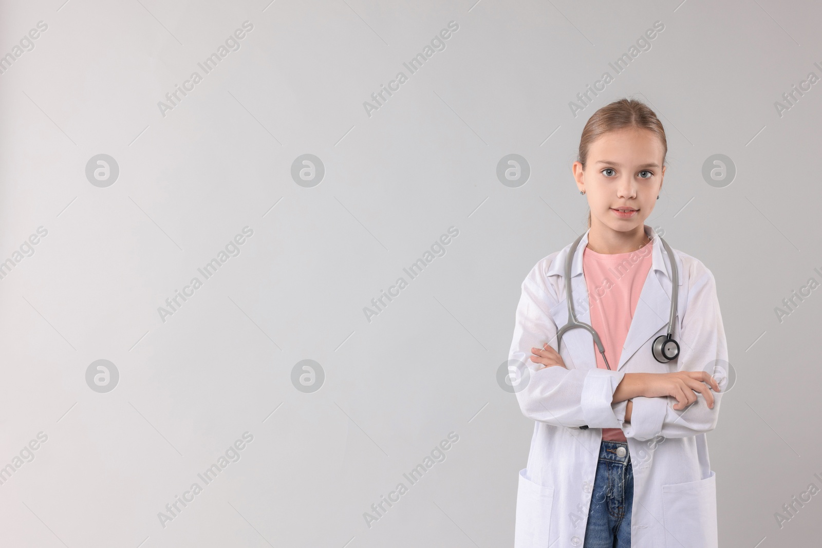 Photo of Girl with stethoscope pretending to be doctor on light grey background, space for text. Dreaming of future profession