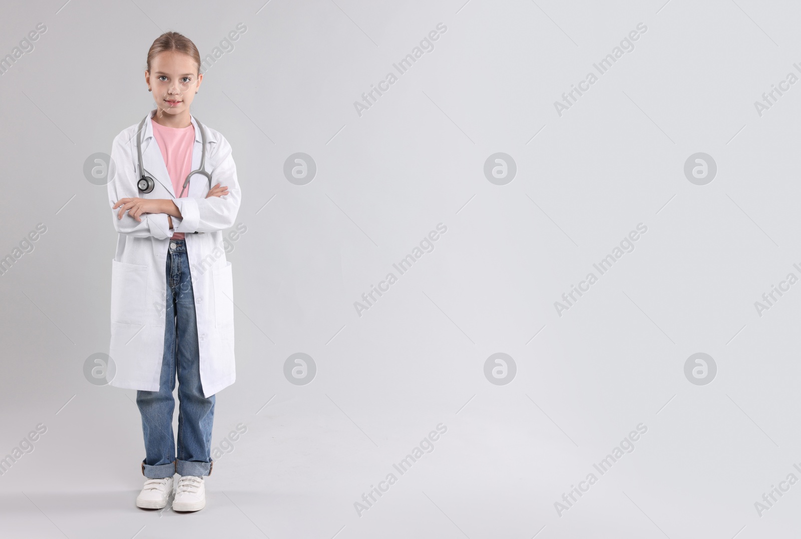 Photo of Girl with stethoscope pretending to be doctor on light grey background, space for text. Dreaming of future profession