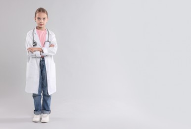 Photo of Girl with stethoscope pretending to be doctor on light grey background, space for text. Dreaming of future profession