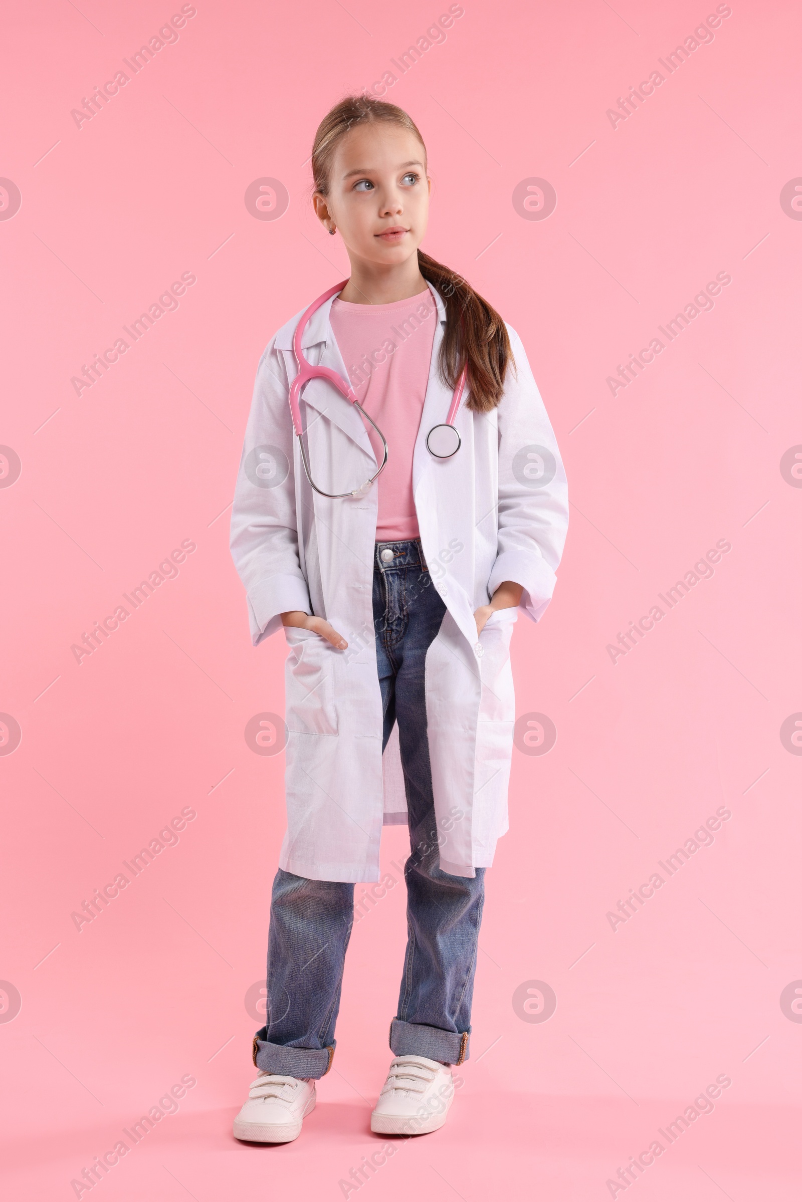 Photo of Girl with stethoscope pretending to be doctor on pink background. Dreaming of future profession