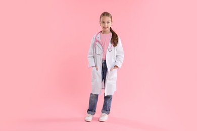 Girl with stethoscope pretending to be doctor on pink background. Dreaming of future profession