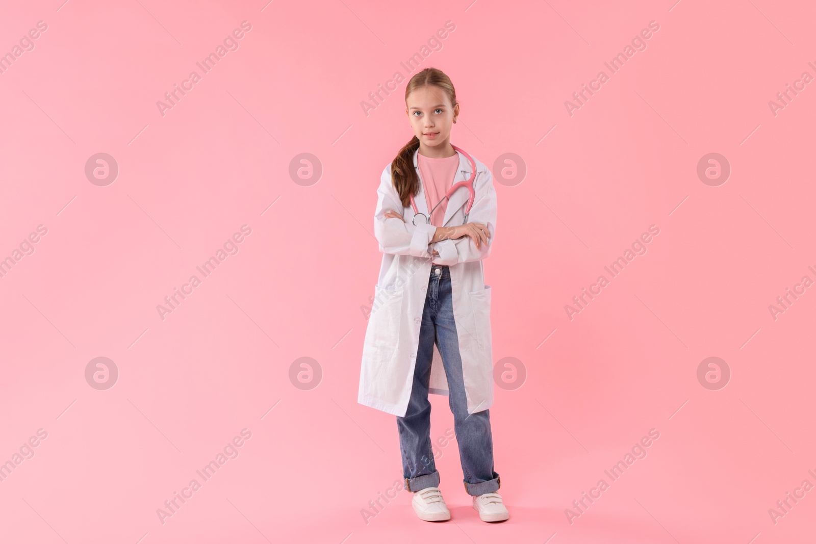 Photo of Girl with stethoscope pretending to be doctor on pink background. Dreaming of future profession