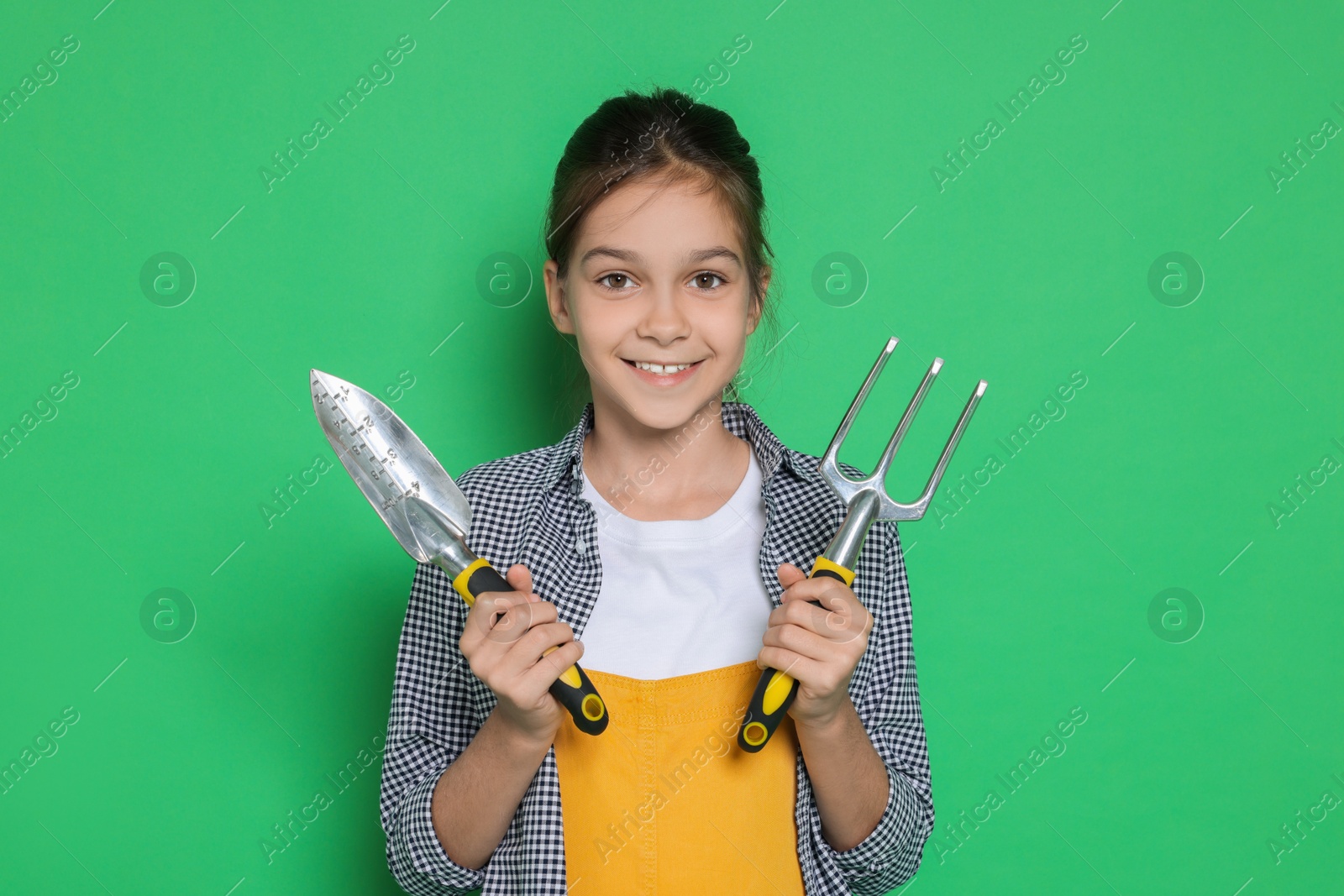 Photo of Girl with tools pretending to be gardener on green background. Dreaming of future profession