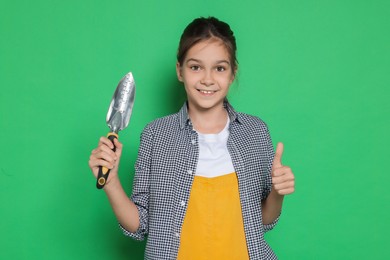 Photo of Girl with trowel showing thumbs up pretending to be gardener on green background. Dreaming of future profession