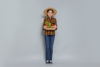 Photo of Girl with straw hat, wooden crate and vegetables pretending to be farmer on light grey background. Dreaming of future profession