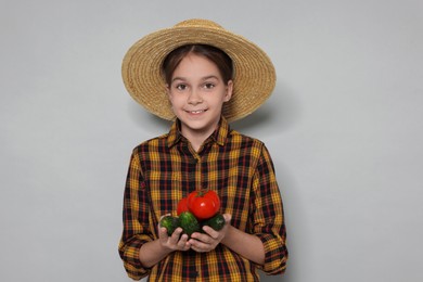 Photo of Girl with straw hat and vegetables pretending to be farmer on light grey background. Dreaming of future profession