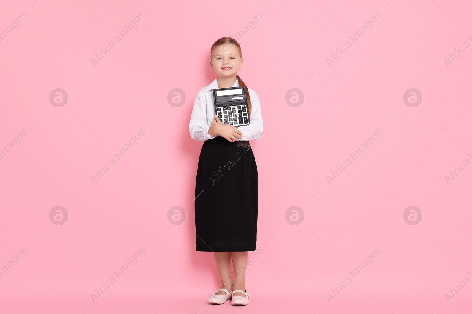 Photo of Little girl with calculator pretending to be accountant on pink background. Dreaming of future profession