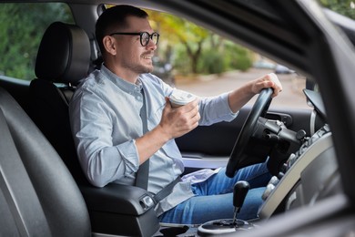 Photo of Man with cup of coffee driving modern car