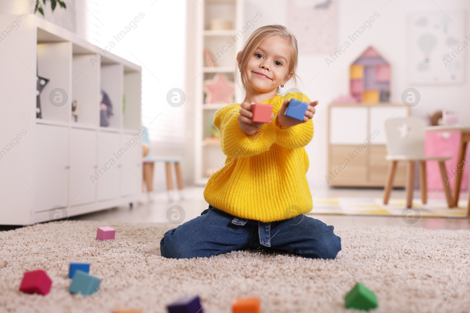 Photo of Cute girl with colorful cubes sitting on carpet at home