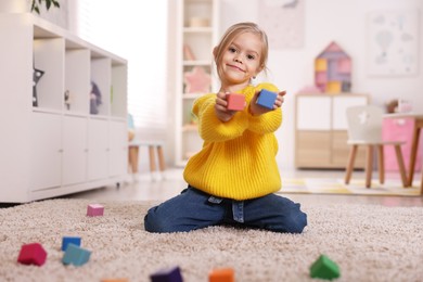 Photo of Cute girl with colorful cubes sitting on carpet at home