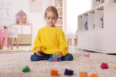 Photo of Cute girl playing with colorful cubes on carpet at home