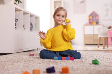 Photo of Cute girl playing with colorful cubes on carpet at home