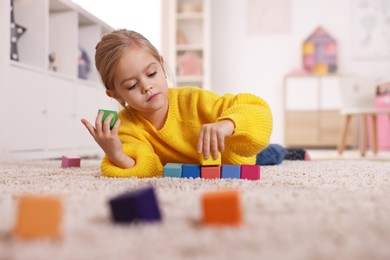 Photo of Cute girl playing with colorful cubes on carpet at home