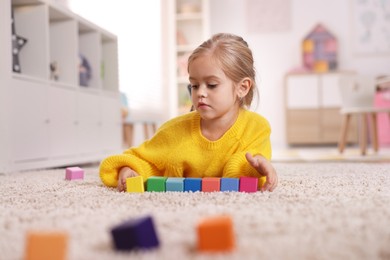 Photo of Cute girl playing with colorful cubes on carpet at home