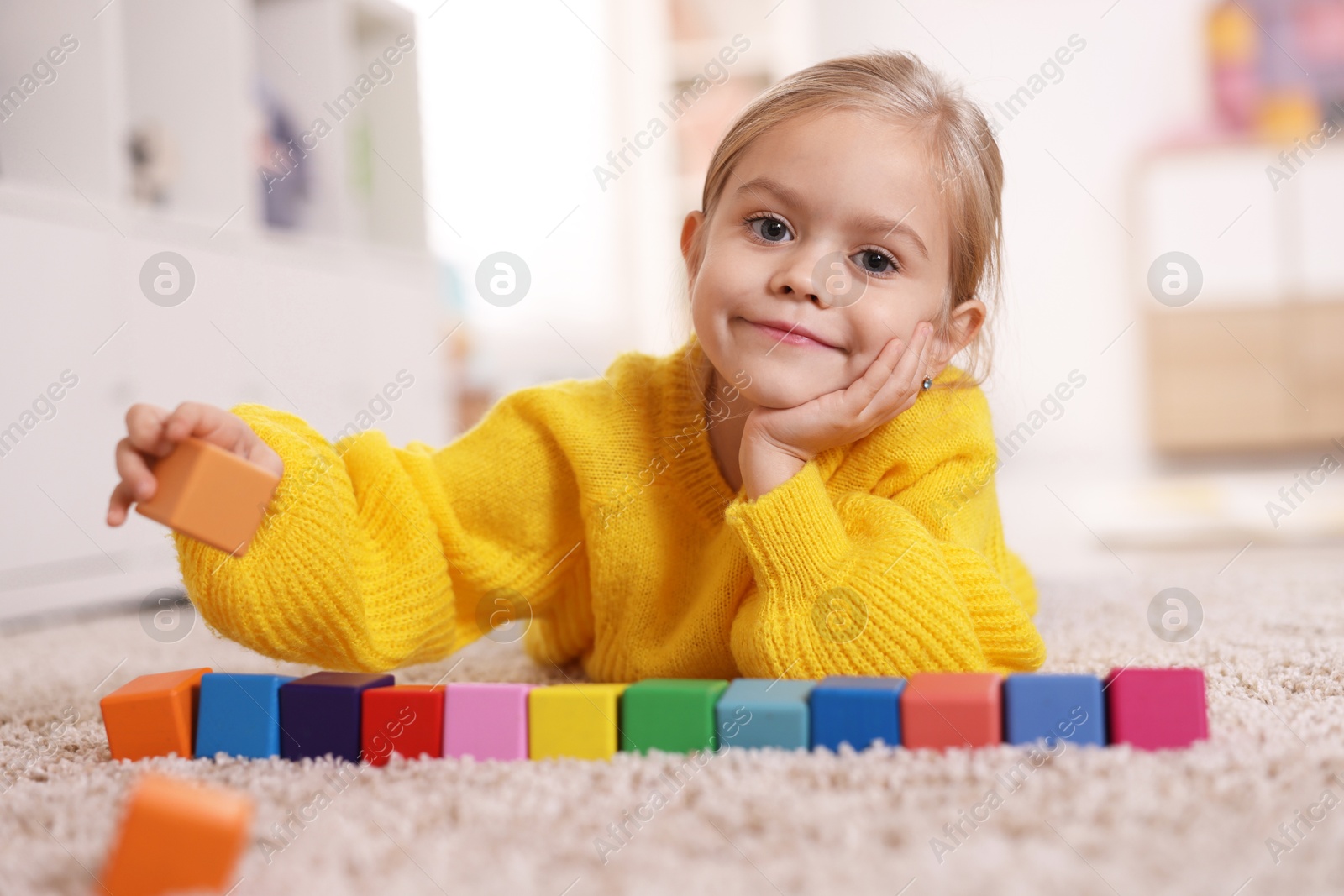 Photo of Cute girl playing with colorful cubes on carpet at home