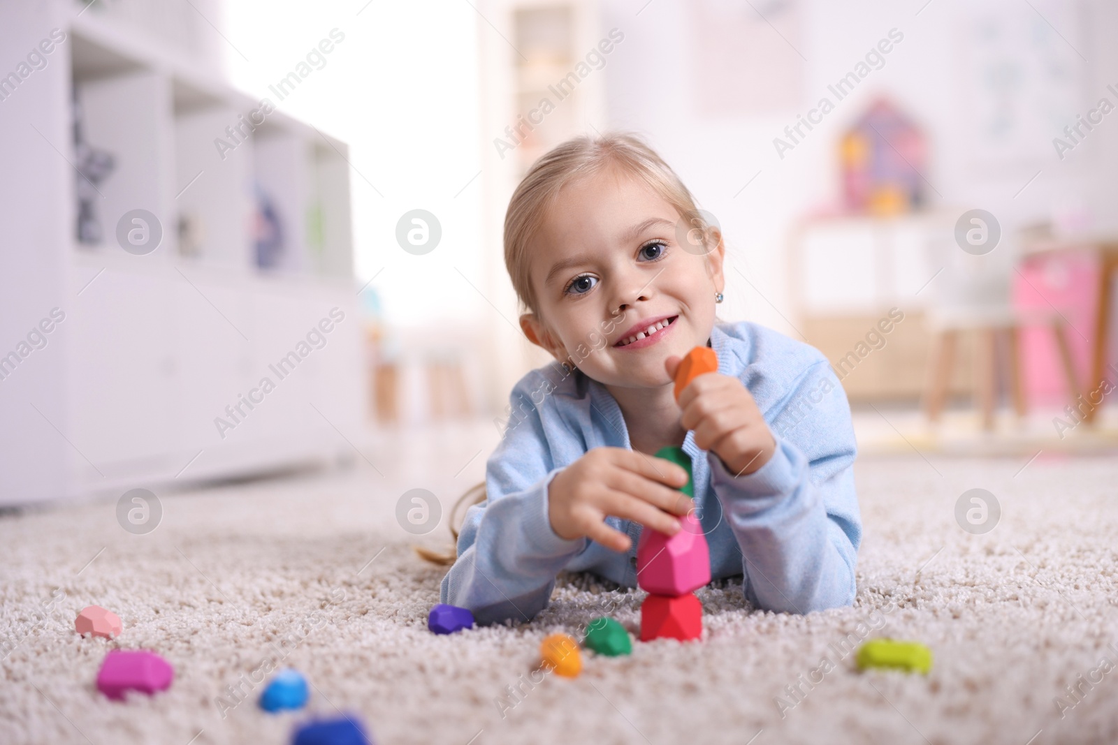 Photo of Smiling girl building tower with balancing stones on carpet at home. Space for text