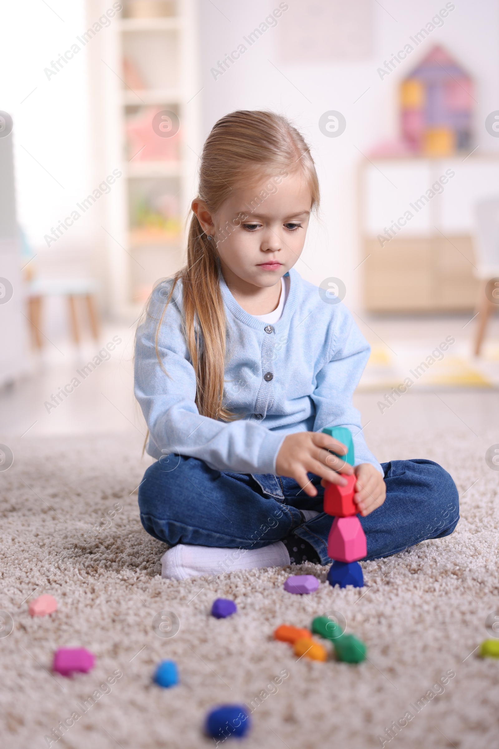 Photo of Cute girl building tower with balancing stones on carpet at home