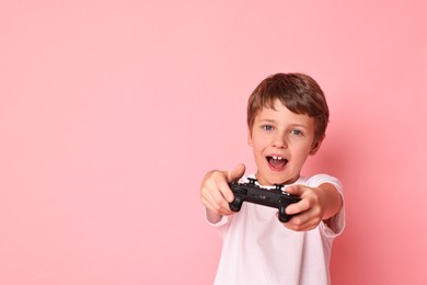 Photo of Happy little boy playing video game with controller on pink background. Space for text