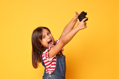 Photo of Emotional little girl with controller on orange background