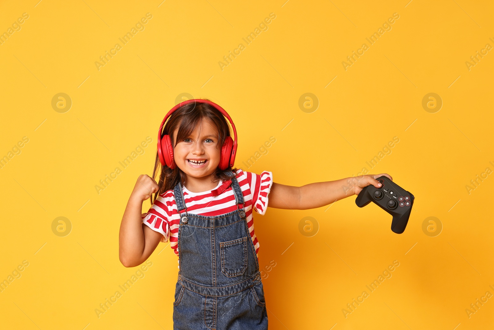 Photo of Smiling little girl in headphones with controller on orange background