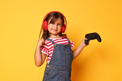 Photo of Cute little girl in headphones with controller on orange background