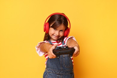 Photo of Happy little girl in headphones playing video game with controller on orange background