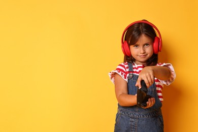 Photo of Cute little girl in headphones playing video game with controller on orange background. Space for text