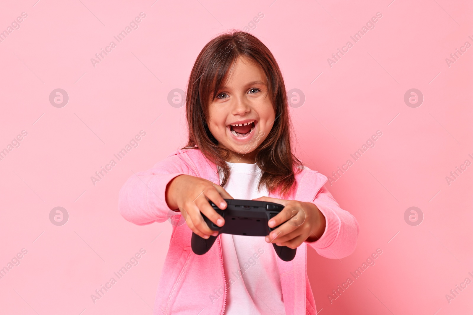 Photo of Happy little girl playing video game with controller on pink background