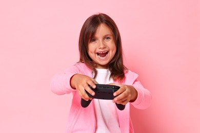 Happy little girl playing video game with controller on pink background