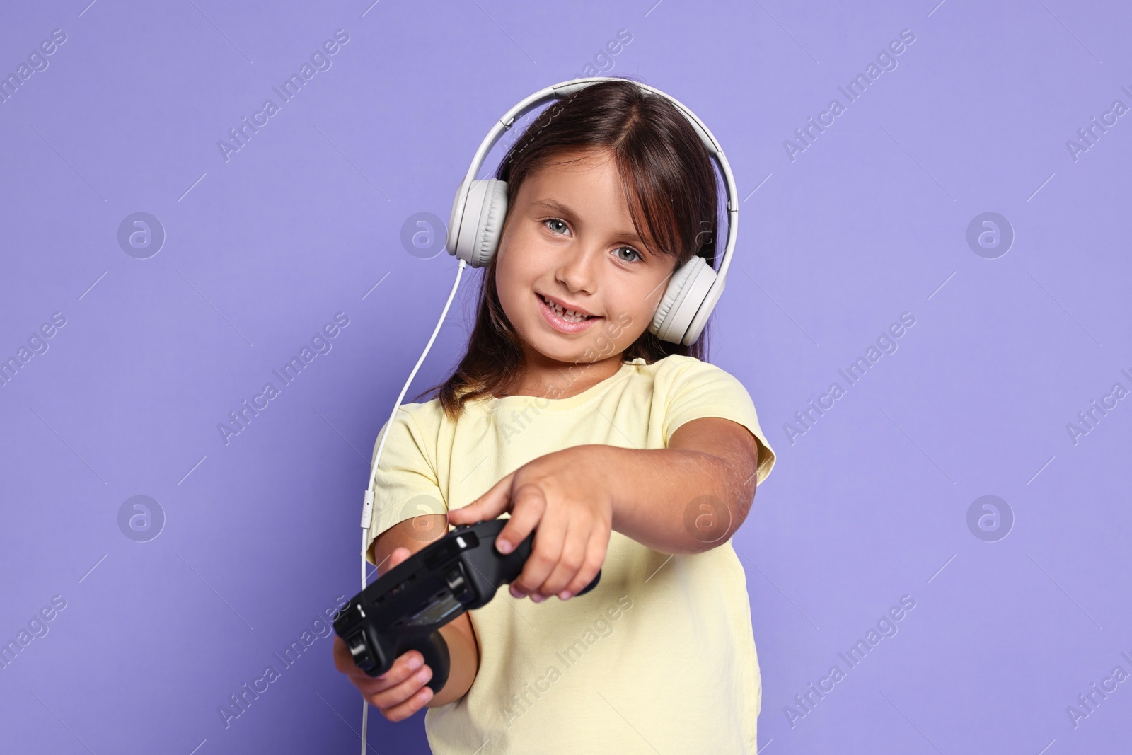 Photo of Happy little girl playing video game with controller on violet background